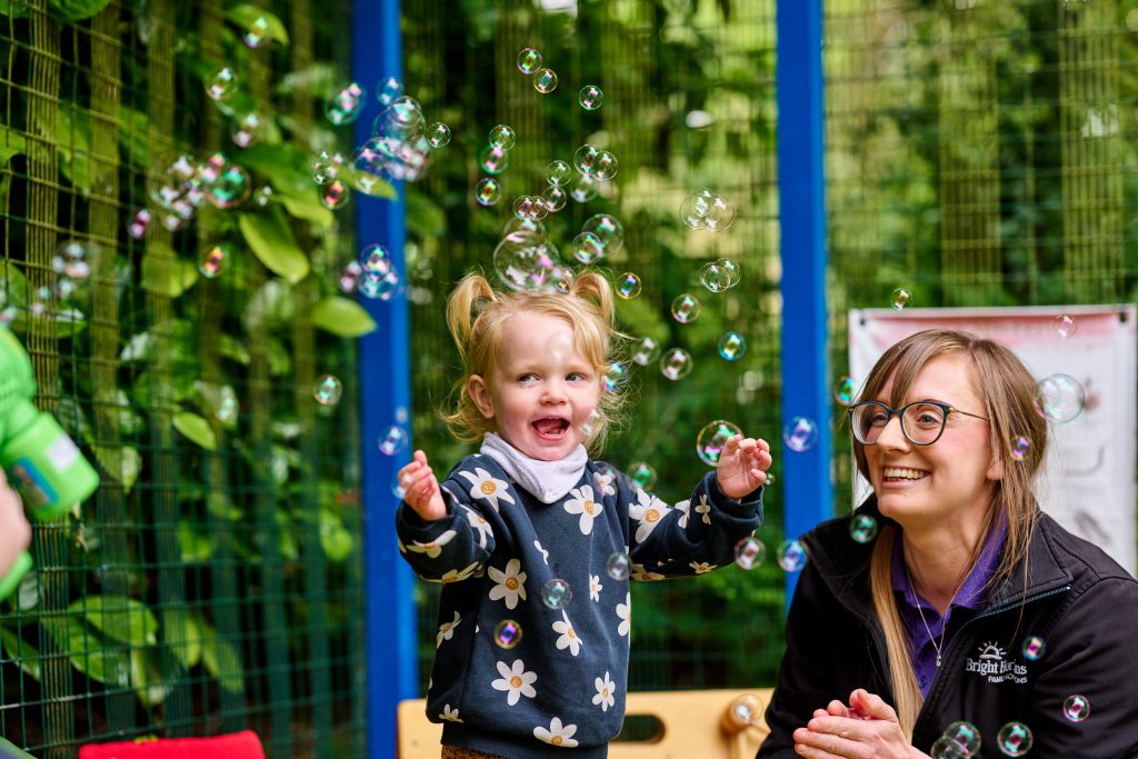 Child playing with bubbles with nursery worker at Bright Horizons nursery